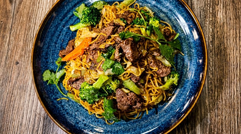 Beef chow mein with broccoli, carrots, and cilantro on a blue plate.