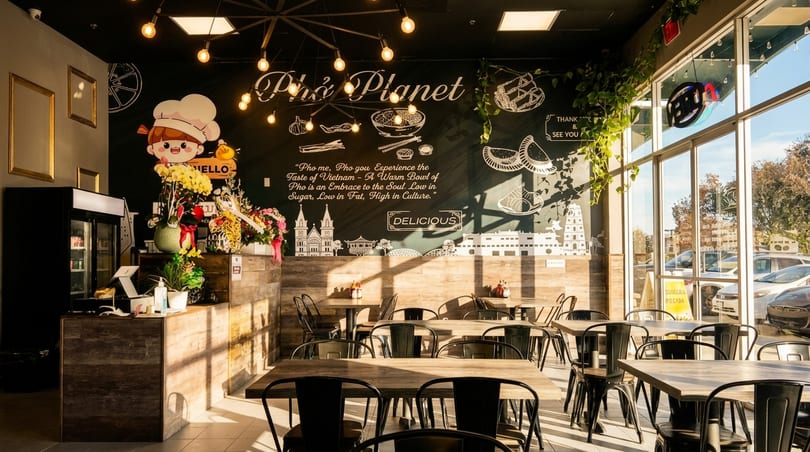 Interior of Pho Planet restaurant with a large mural, wooden tables, and natural light.