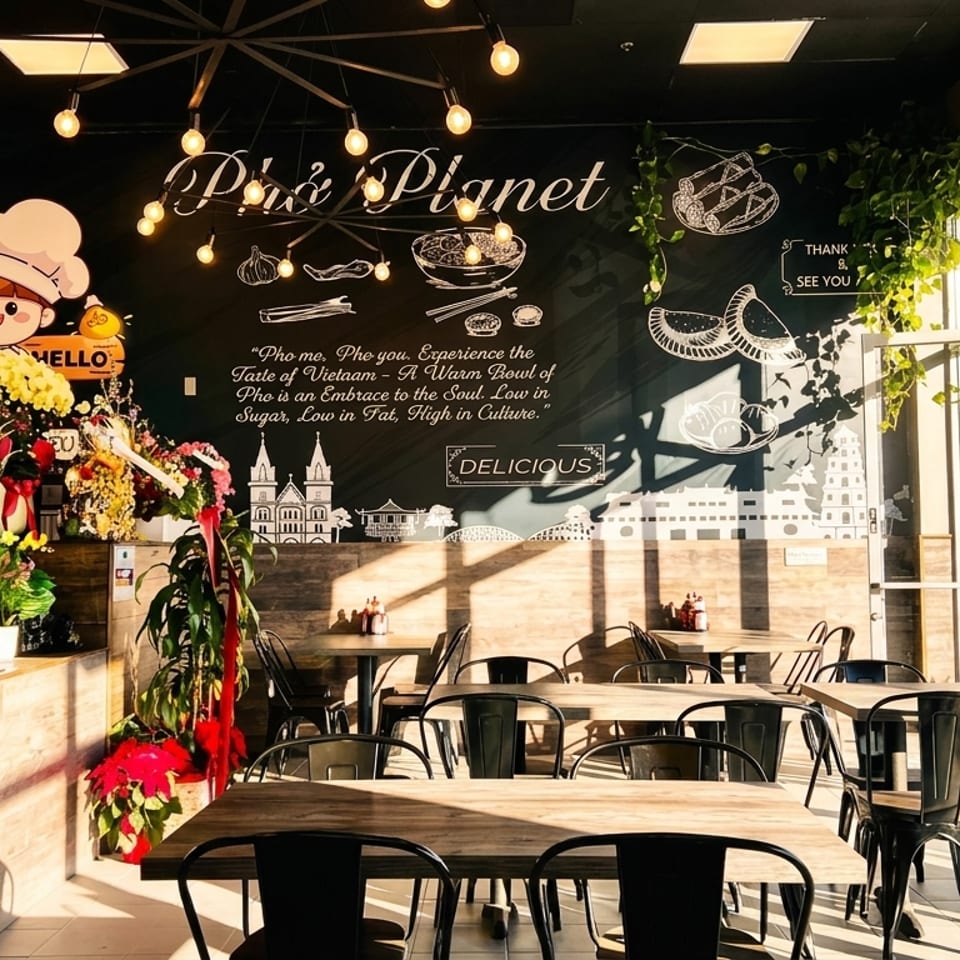 Interior of Pho Planet restaurant with wooden tables, black chairs, and a large mural on a dark wall.