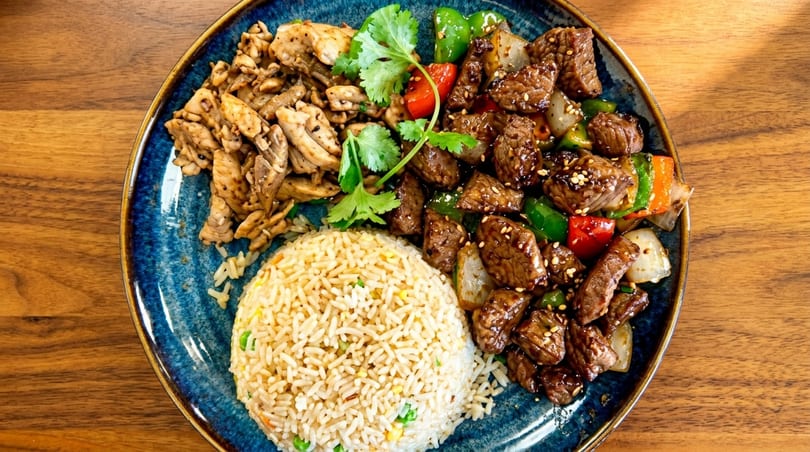 A blue plate with fried rice, grilled chicken, and beef stir-fry with peppers and onions.
