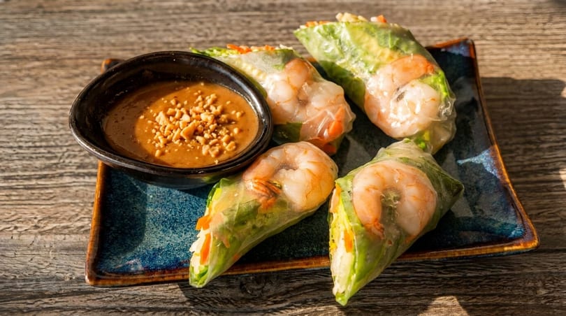 Four fresh shrimp spring rolls with peanut dipping sauce on a blue plate.